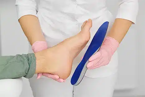 doctor holding a blue insole up to a patients bare foot