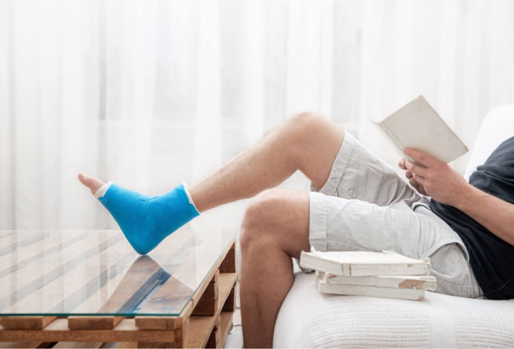  Man sitting with his leg elevated in a cast, recovering from a foot or ankle injury, indicating a need for podiatric care.