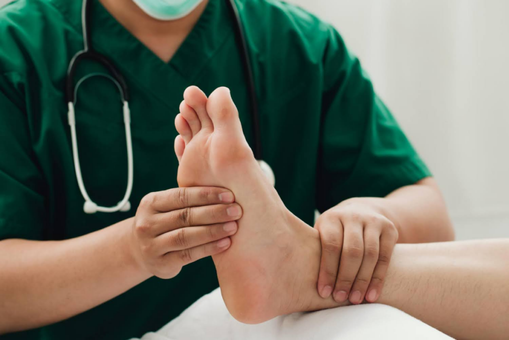 Medical professional in green scrubs examining a patient's foot, assessing for neuropathy or other foot-related issues.