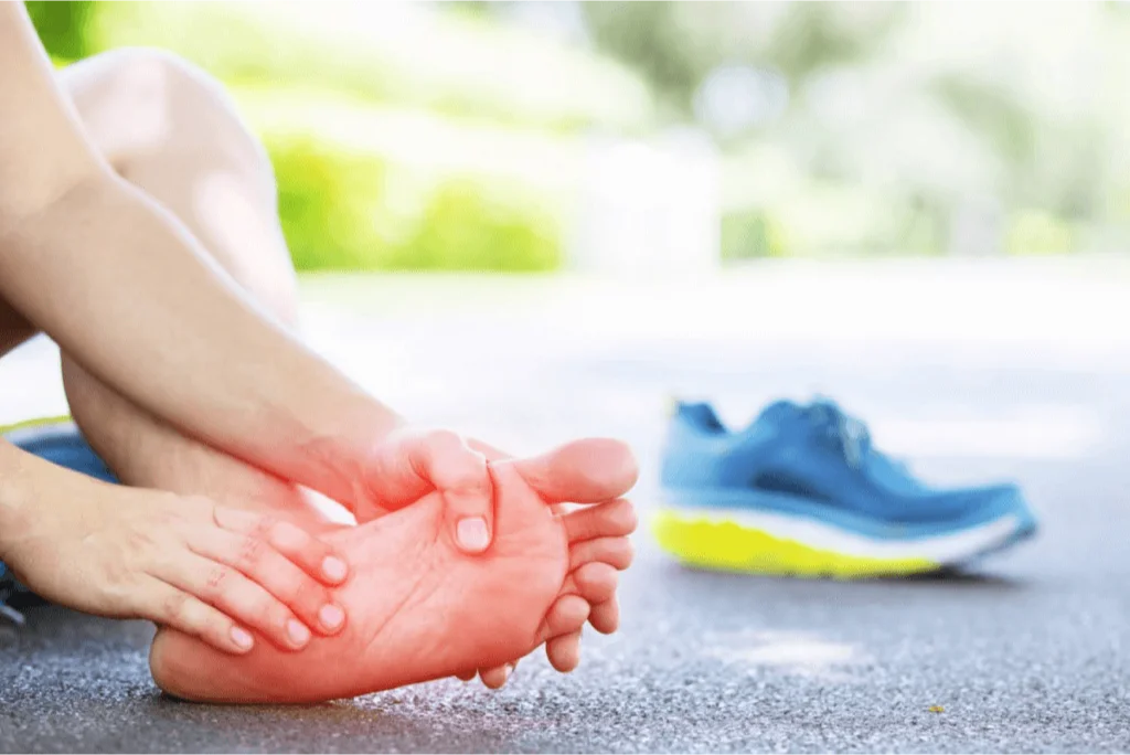 Runner holding their foot in pain on a running track, likely experiencing foot discomfort due to neuropathy.