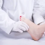 A doctor wearing gloves holding a patient's foot during a clinical examination.