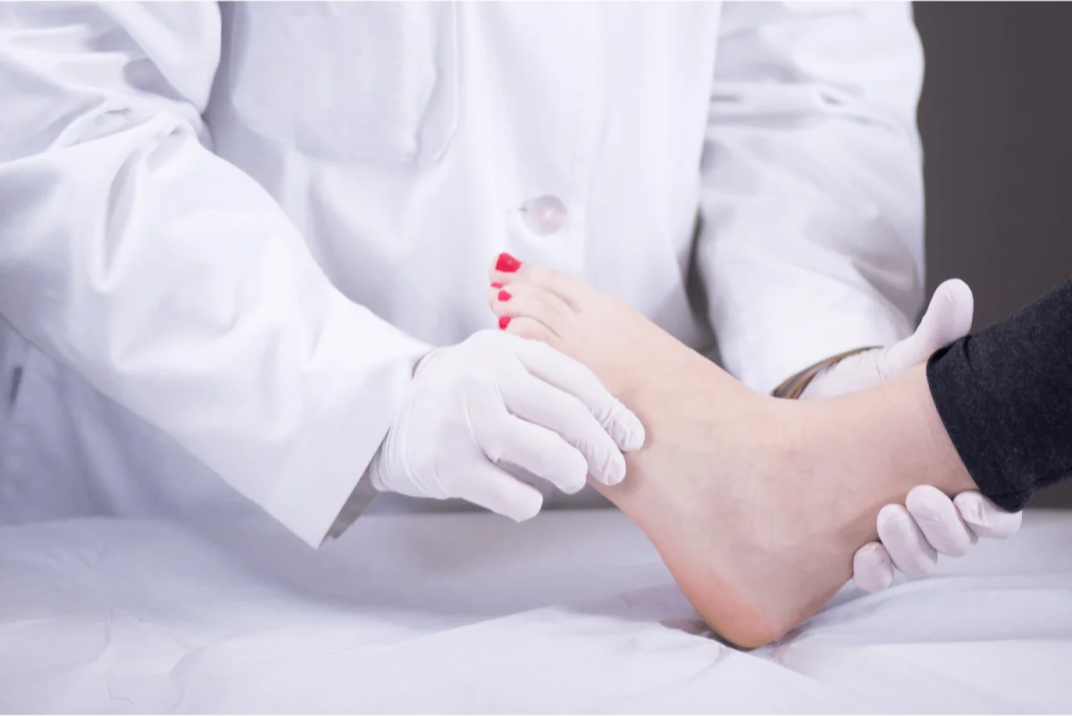 A doctor wearing gloves holding a patient's foot during a clinical examination.